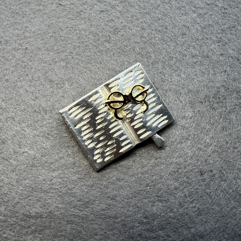 Broșă în formă de carte cu ochelari, email deschis gri și auriu, metal argintiu 35×26 mm