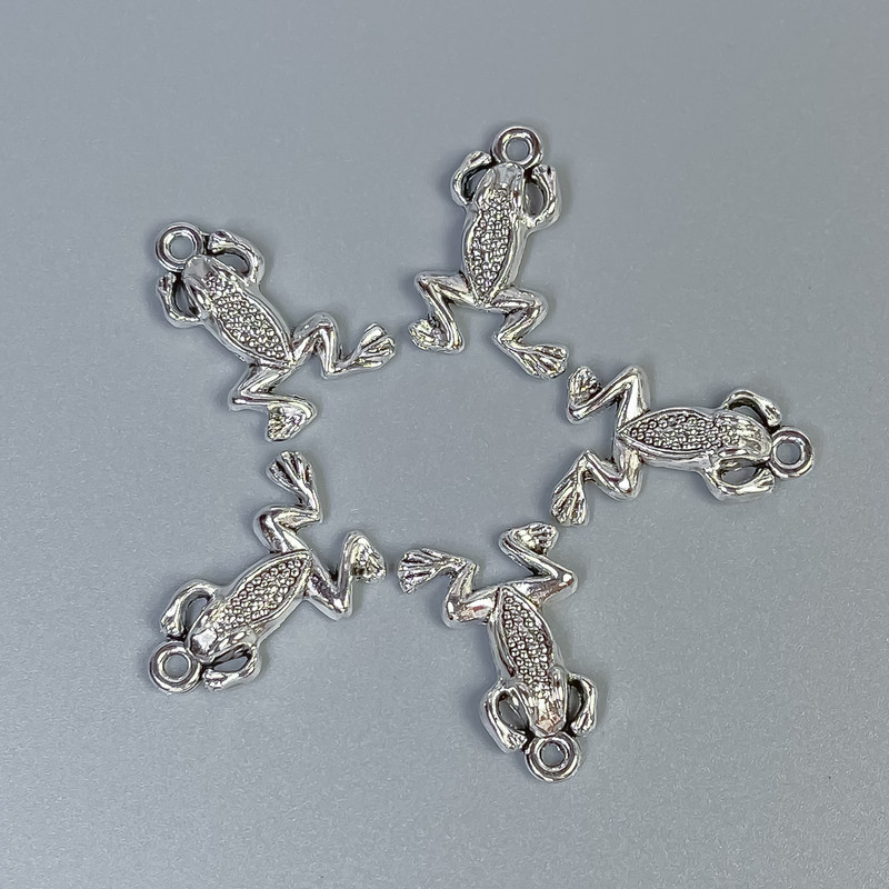 Pandantiv broscuță, culoare argintie, dimensiuni 20x13x3 mm +/- gaură de 1,5 mm +/- ambalare 20 g (~18 buc.)